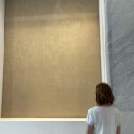 A visitor standing before an engraved panel by Afro Basaldella at Palazzo Marignoli